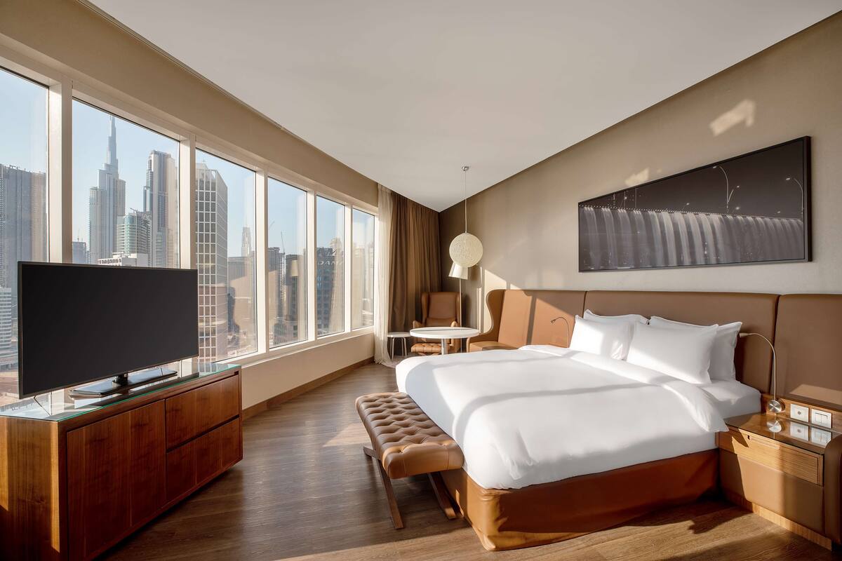 A modern hotel room with a large bed, a television on a wooden cabinet, a small table, and a chair.