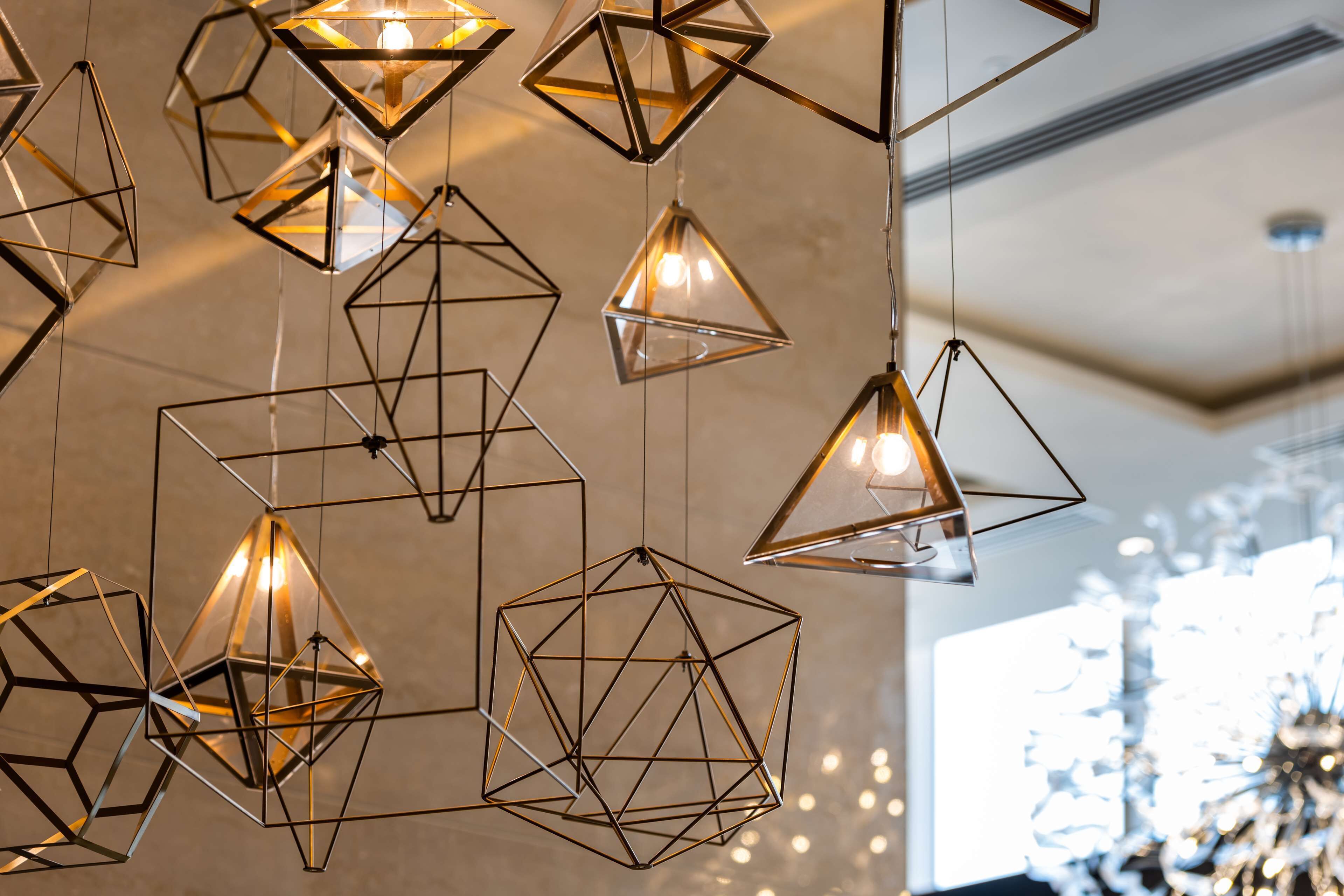 Uma série de luminárias pendentes geométricas com fonte de luz quente visível em cada uma.