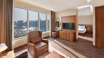 Quarto de hotel moderno com uma janela ampla com vista para a cidade, um espaço de estar confortável, uma televisão de tela plana e uma cama bem arrumada.