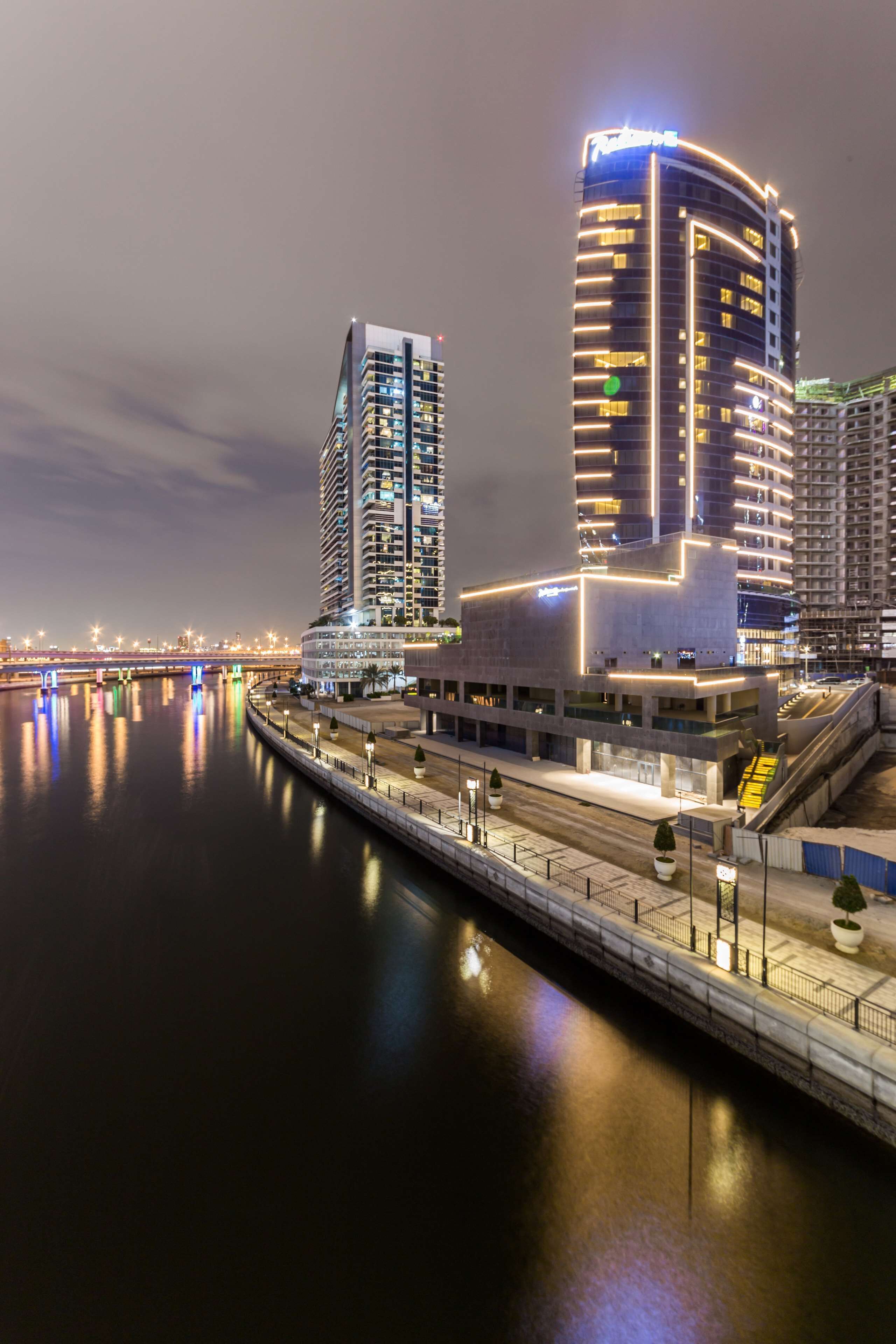 Um hotel moderno com fachada curva, vista para a orla marítima e uma ponte ao fundo.