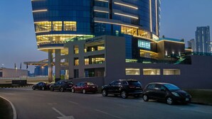Een hoog hotel met een gebogen gevel, verlichte reclameborden en een parkeerplaats met meerdere auto's.