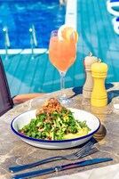 A table with a meal, a drink, and a poolside view.