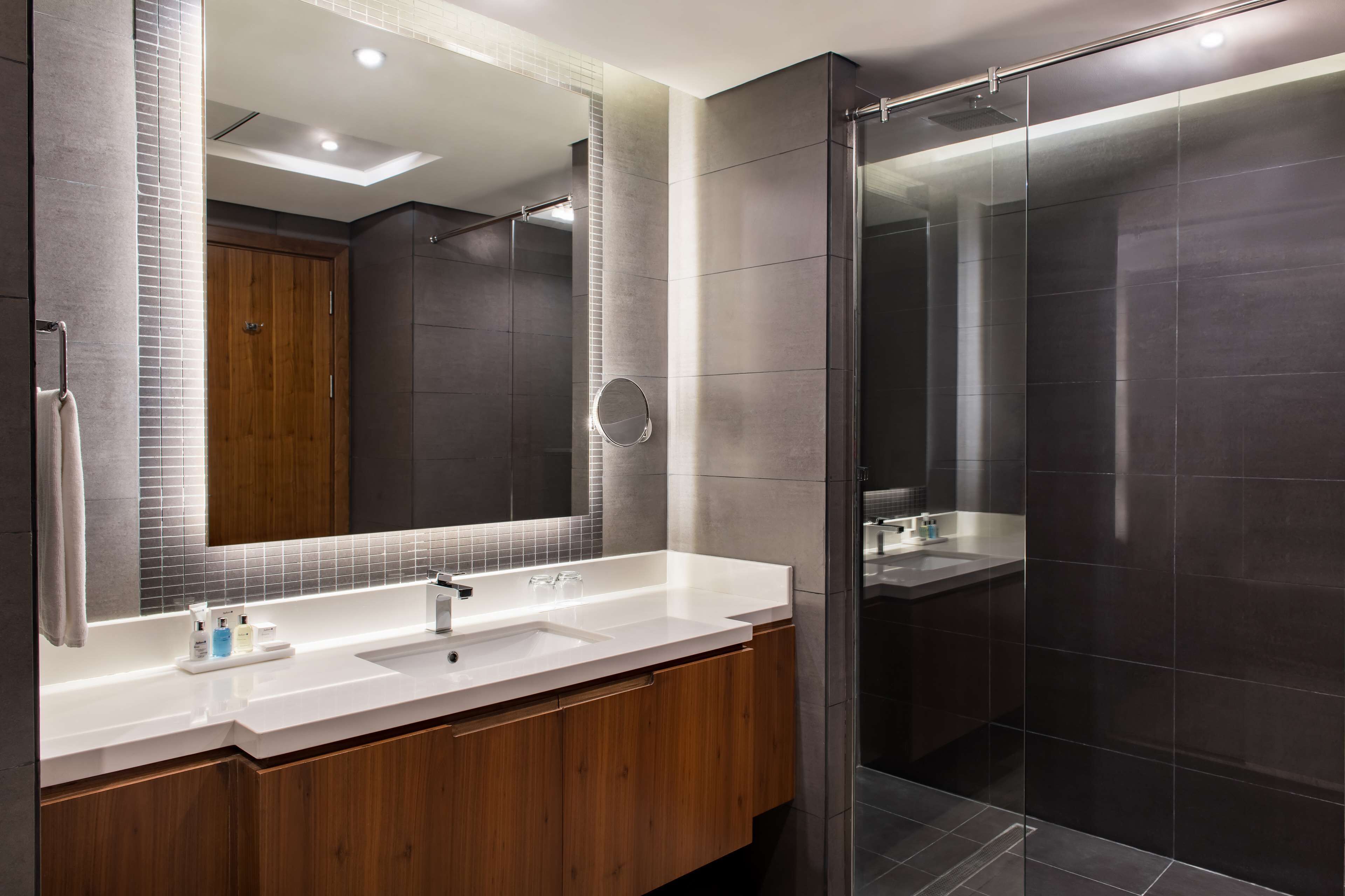 Une salle de bain moderne avec un grand miroir, deux vasques, des meubles en bois et une cabine de douche en verre.