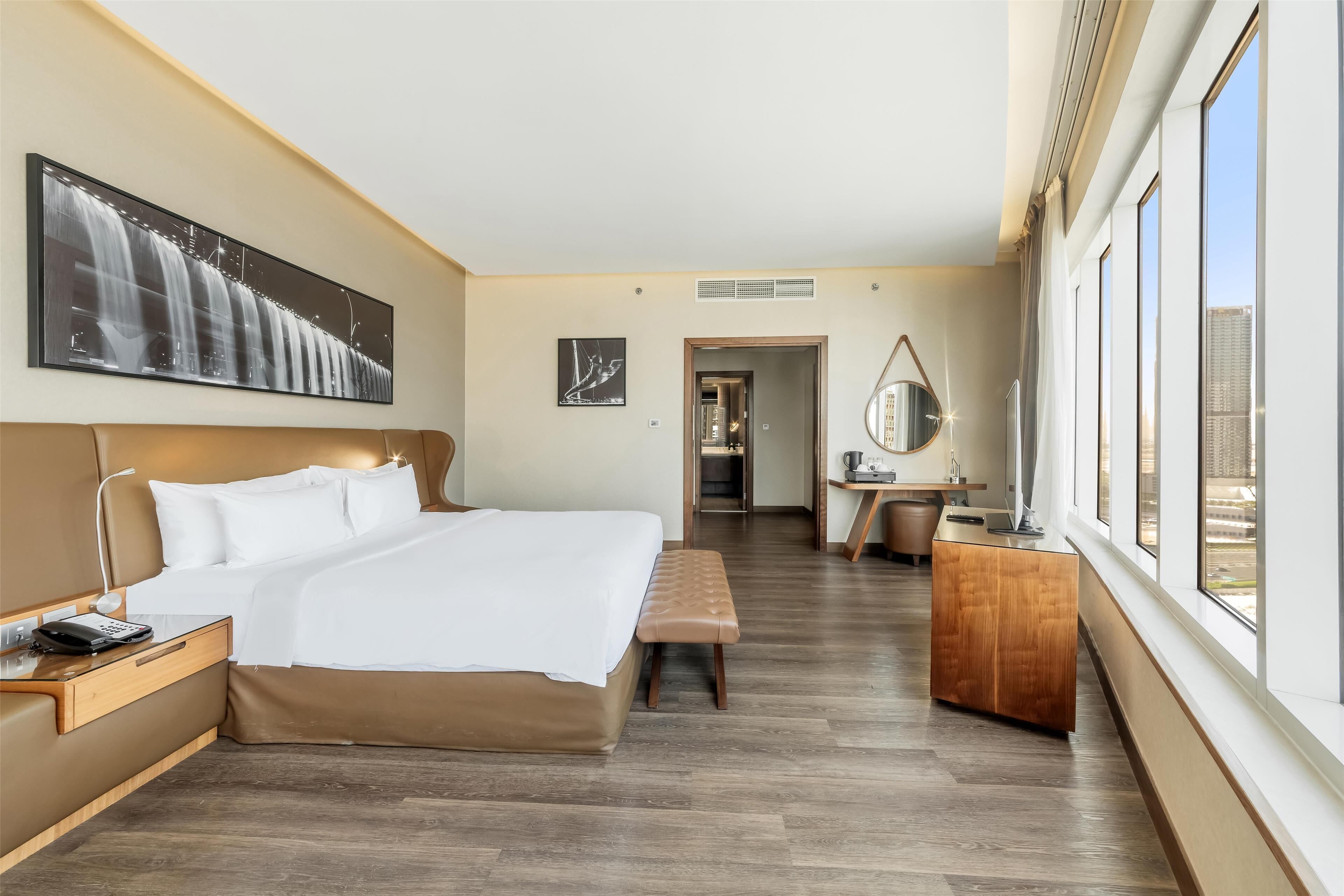 Et hotelværelse med en stor seng, et skrivebord, en stol og et vindue med udsigt over byen.