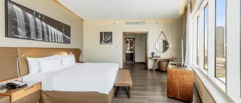 A hotel room with a large bed, a desk, a chair, and a window with a city view.