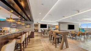 A modern bar area with wooden flooring, bar stools, and pendant lighting.