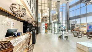 Een ruime lobby met een marmeren receptiebalie, grote ramen en modern meubilair.