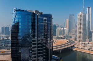 A modern high-rise building with a curved glass facade, surrounded by other tall buildings and a river.