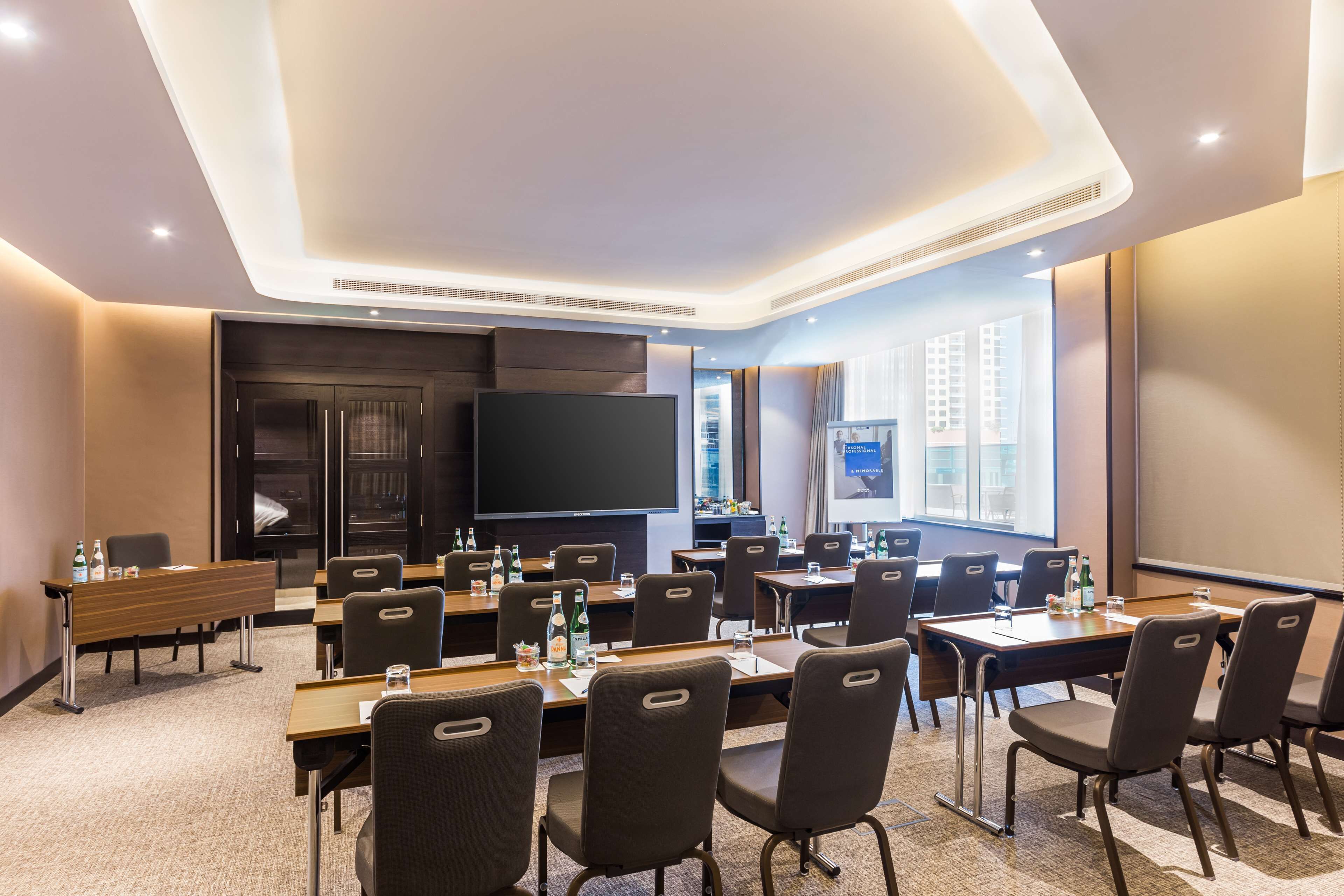 A conference room with multiple tables and chairs, a large flat-screen TV, and a projector screen.