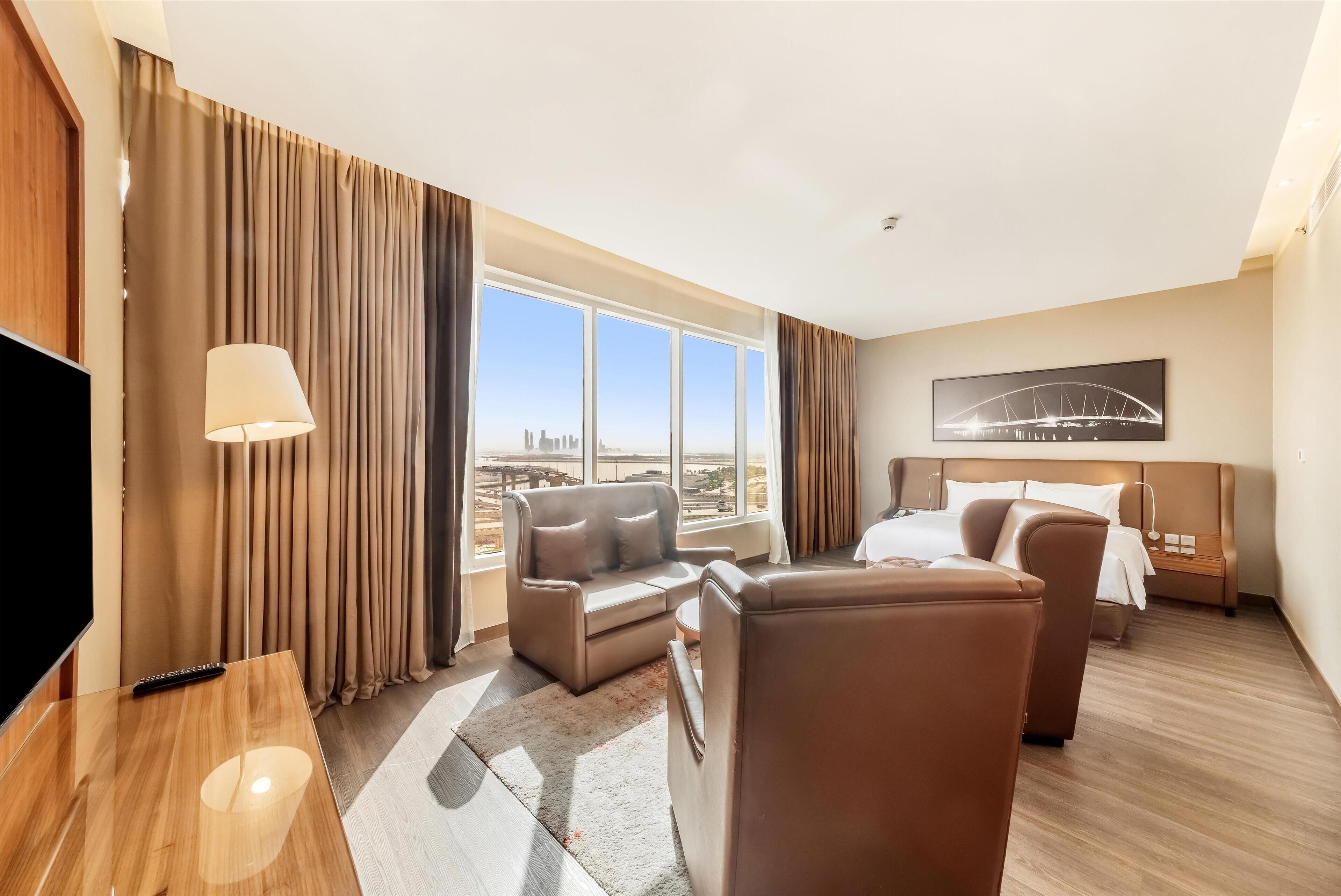 Habitación de hotel con un ventanal grande, un sofá, una silla, una cama y un televisor.