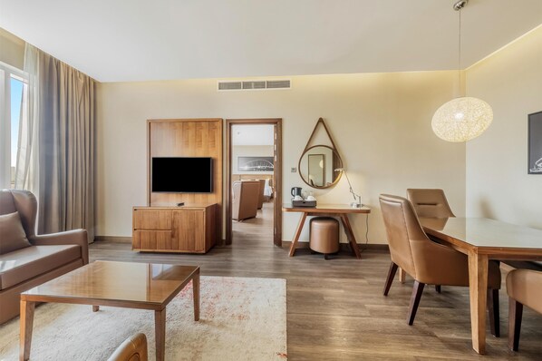 A modern living room with a flat-screen TV, wooden furniture, a dining table, and a large mirror.