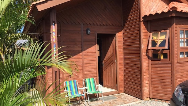 A wooden building with a garage door, two folding chairs, and a car parked in front. - Bangalôs Pico do Avião em frente à IIha do Campeche (Florianópolis)