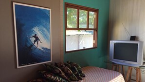 A bedroom with a bed, a poster, a window, and a television. - Bangalôs Pico do Avião em frente à IIha do Campeche (Florianópolis)