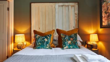 Uma cama com duas almofadas florais, uma cabeceira de madeira e duas luminárias de cabeceira.