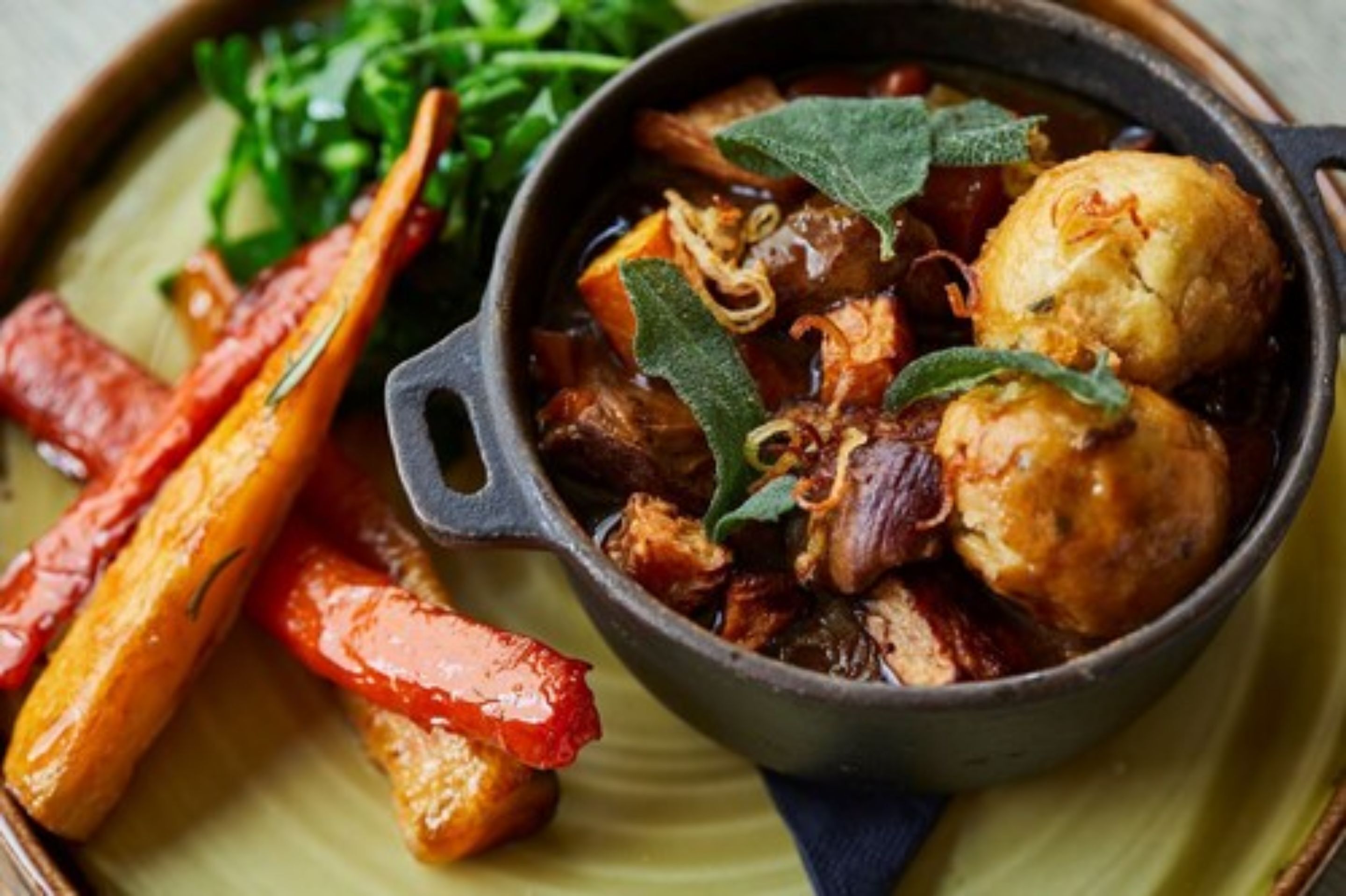 A dish with roasted vegetables and meat in a cast iron skillet, served on a plate with greens.