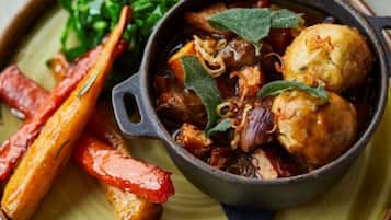 A dish with roasted vegetables and meat in a cast iron skillet, served on a plate with greens.