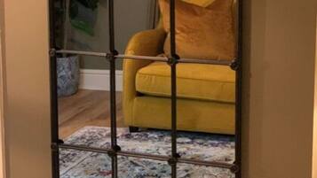 A room with a yellow sofa, a patterned rug, and a potted plant.