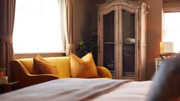 A hotel room with a bed, a yellow sofa, a wooden wardrobe, and a window with curtains.