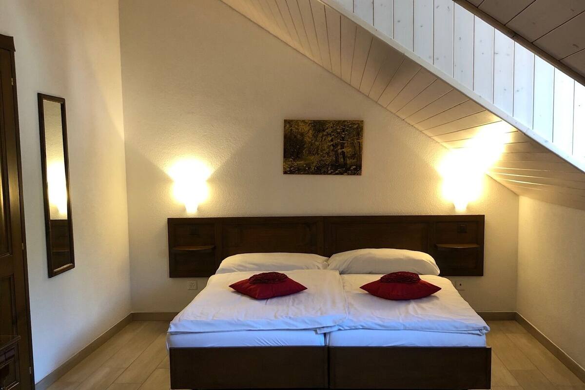 A bedroom with a large bed, two bedside lamps, a painting on the wall, and a wooden ceiling.