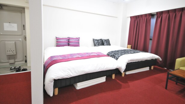 A hotel room with two beds, red curtains, and a small table. - GATE80 nagai stadium (Osaka)