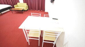 A hotel room with a white table and chairs, a yellow armchair, a bed, and red curtains. - GATE80 nagai stadium (Osaka)