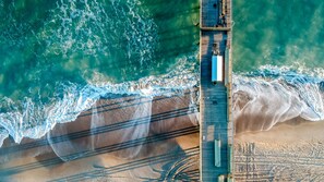 An aerial view of a pier extending into the ocean with waves crashing onto the shore. - Classic Waterfront Cottage Private Pool Near Beach Water Views (Emerald Isle)