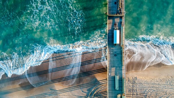 An aerial view of a pier extending into the ocean with waves crashing onto the shore.