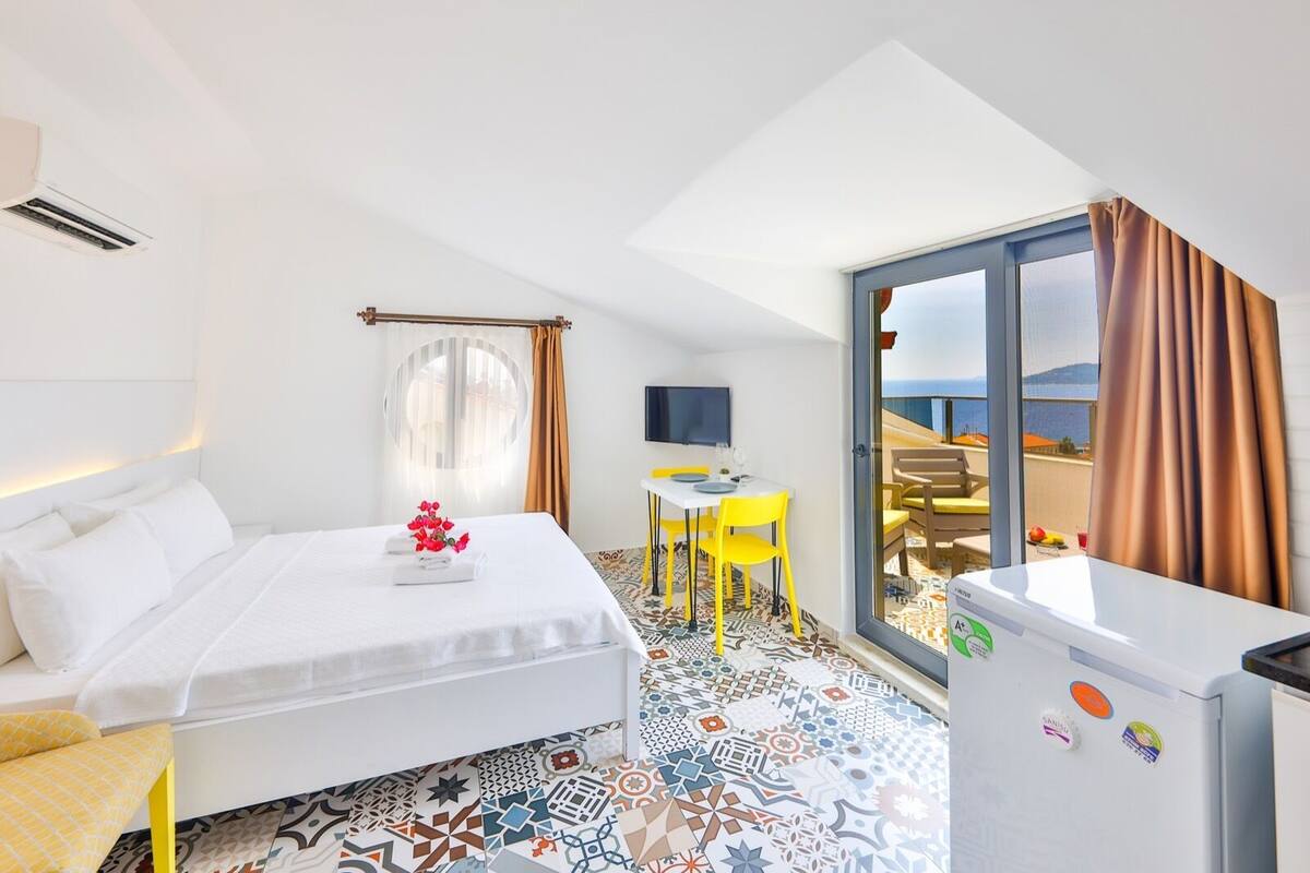 A hotel room with a bed, a desk, a chair, a small table, a TV, and a balcony with a view.