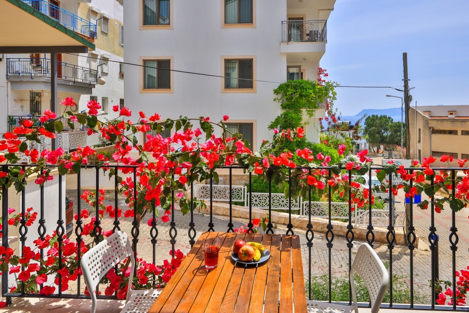 A balcony with a wooden table, red flowers, and a view of buildings.