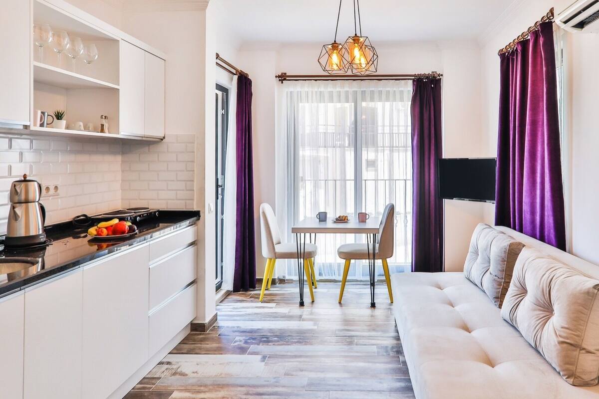 A modern kitchen with white cabinets, a dining area with a table and chairs, and a living area with a sofa.