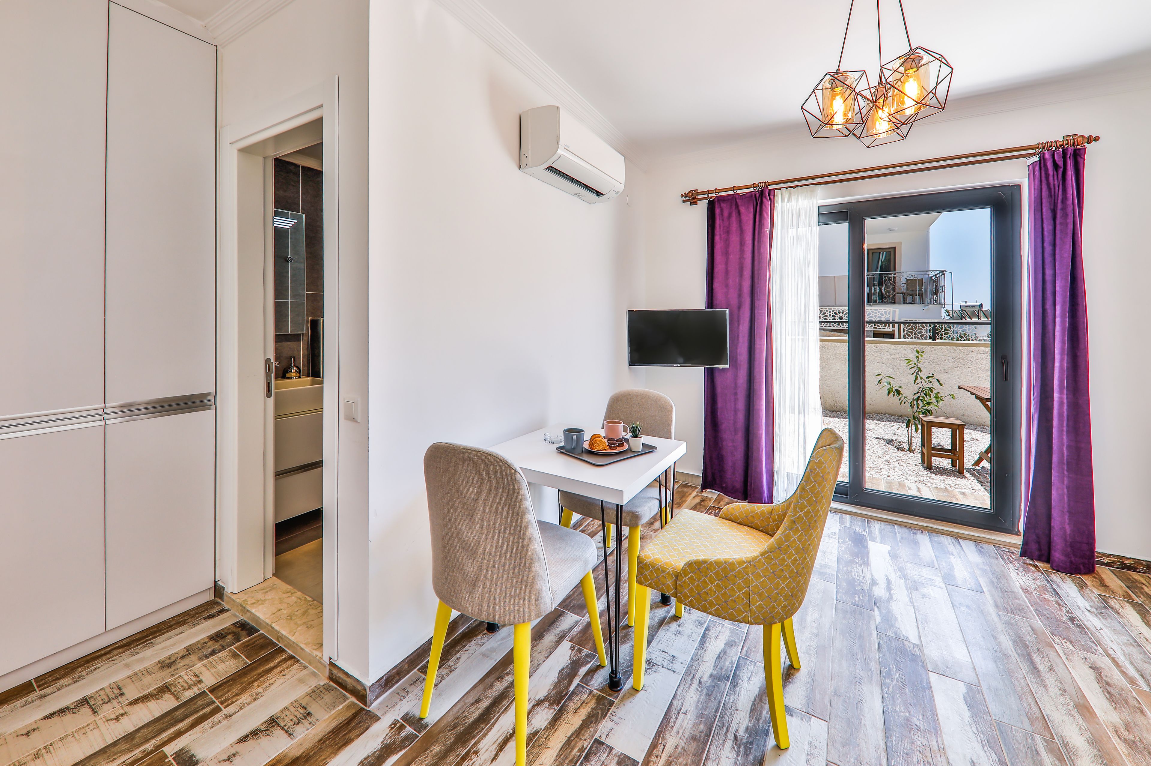 A compact room with a dining table, chairs, a TV, and a sliding glass door to an outdoor area.