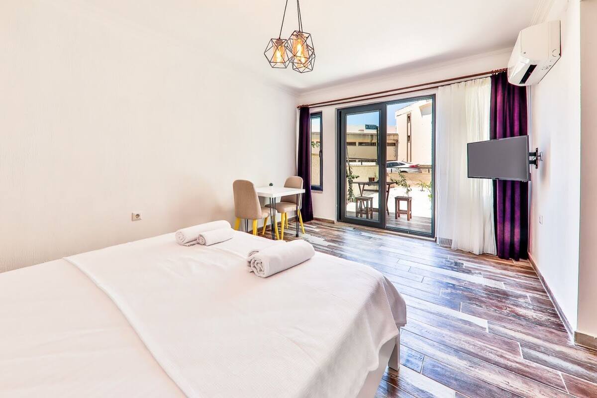 A hotel room with a bed, a desk, a chair, a TV, and a balcony with a view.