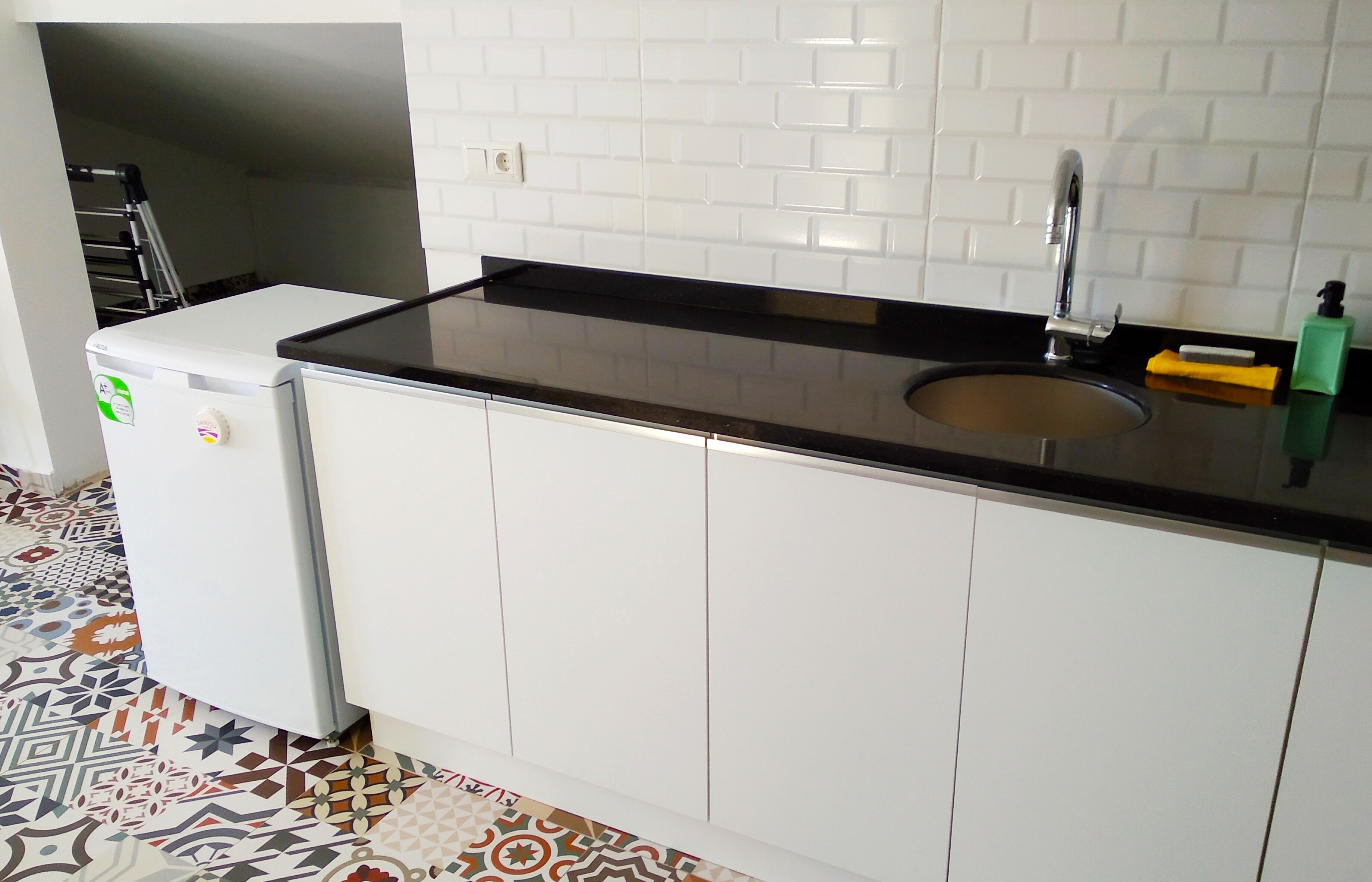 A kitchen with white cabinets, a black countertop, a sink, and a small refrigerator.