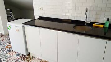 A kitchen with white cabinets, a black countertop, a sink, and a small refrigerator.
