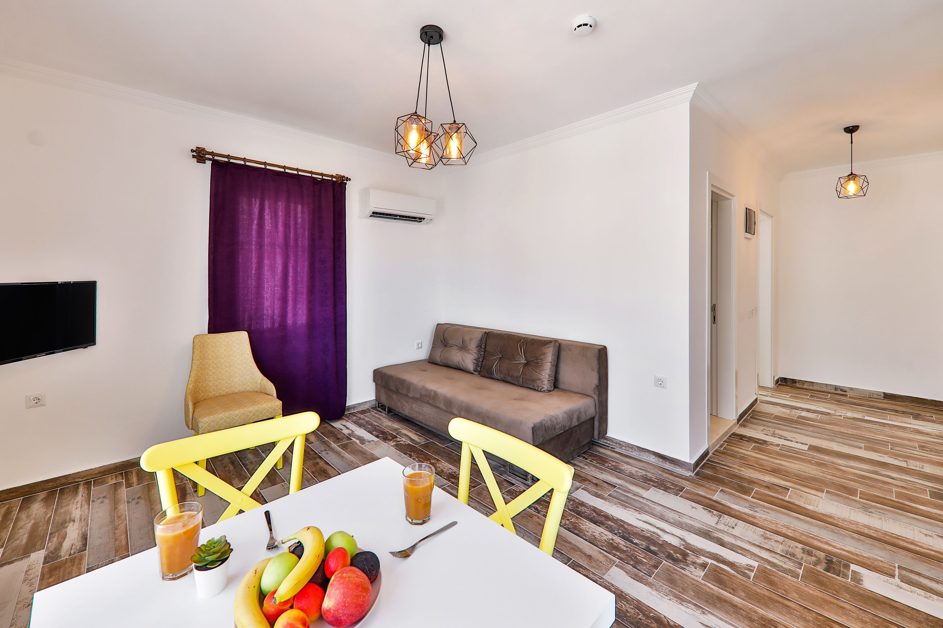 A modern living room with a dining table, yellow chairs, a brown sofa, and a purple curtain.