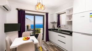 A modern kitchen with white cabinets, a black countertop, and a view of the sea through the sliding glass door. - Kas Sanisu Pansiyon (Kas)
