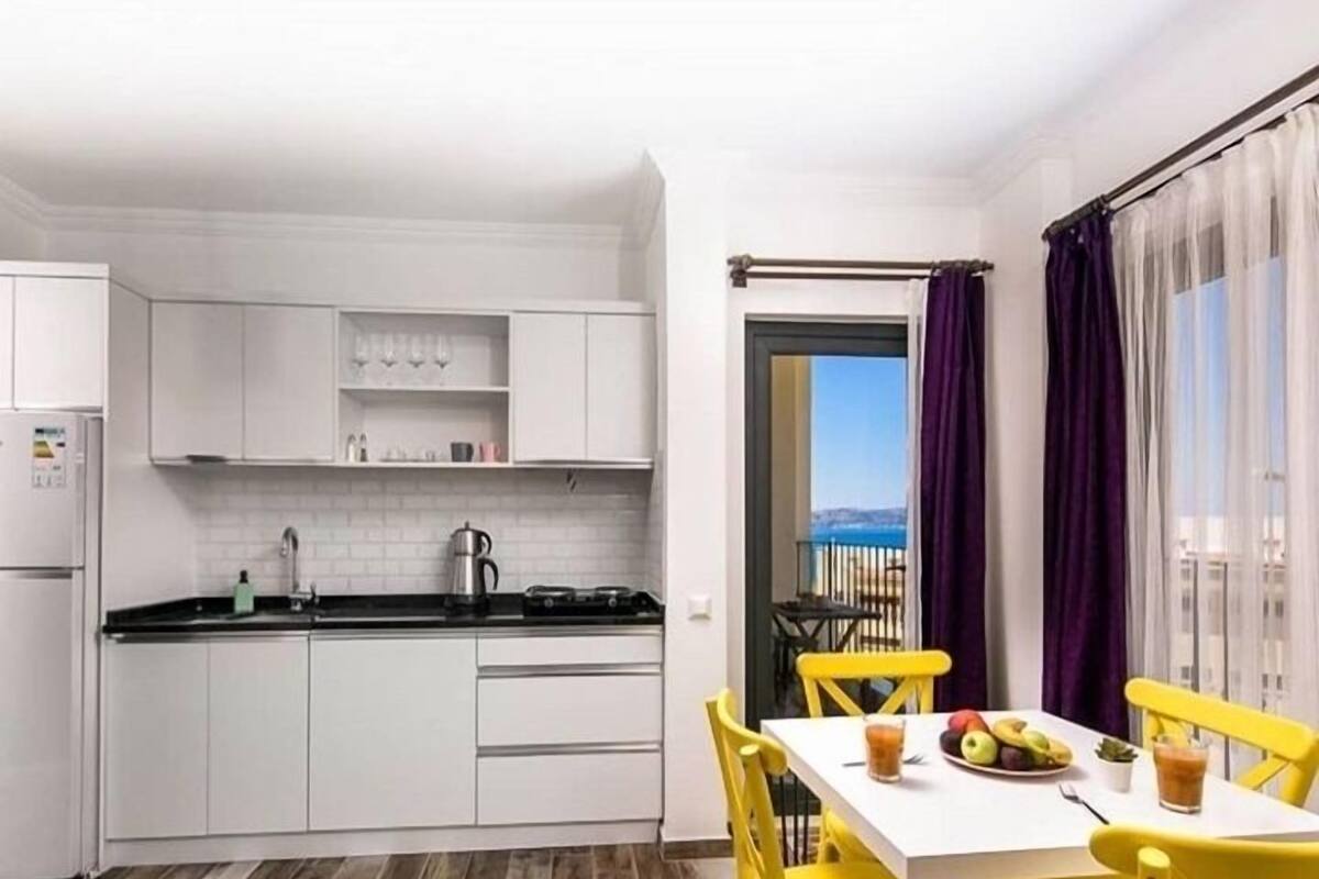 A modern kitchen with white cabinets and a dining area with yellow chairs.