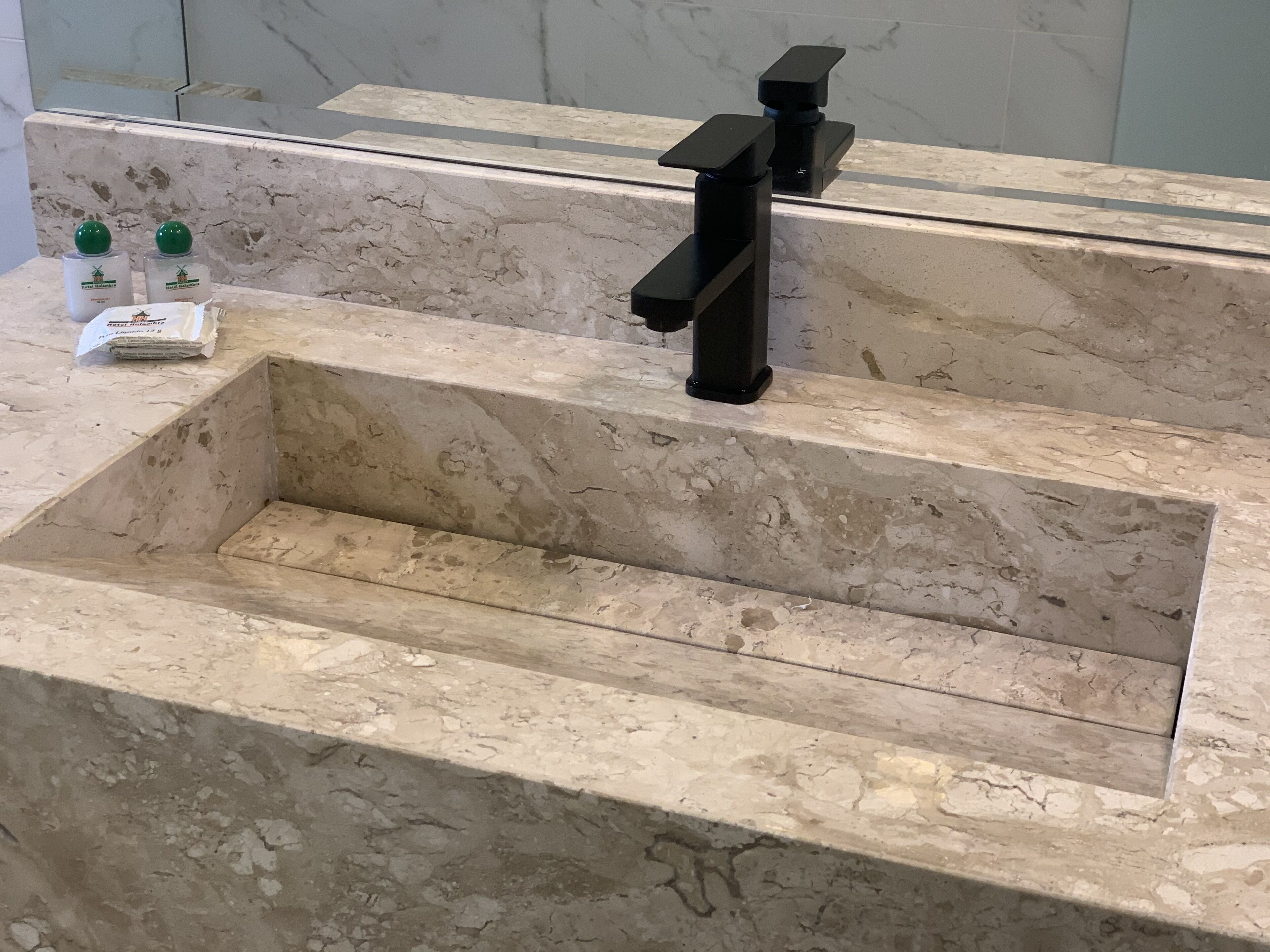 A bathroom with a marble sink, a mirror, and two green bottles on the counter.