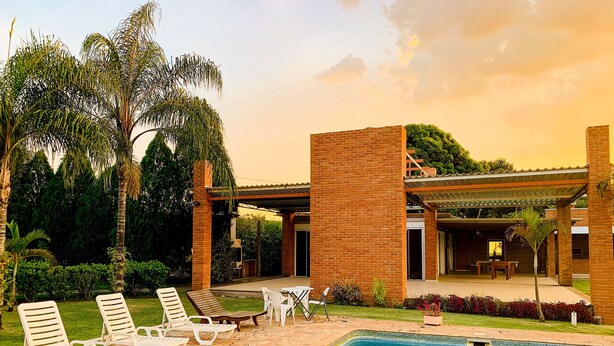 A pool area with lounge chairs, a brick building, and palm trees. - Parque Hotel Holambra (Holambra)