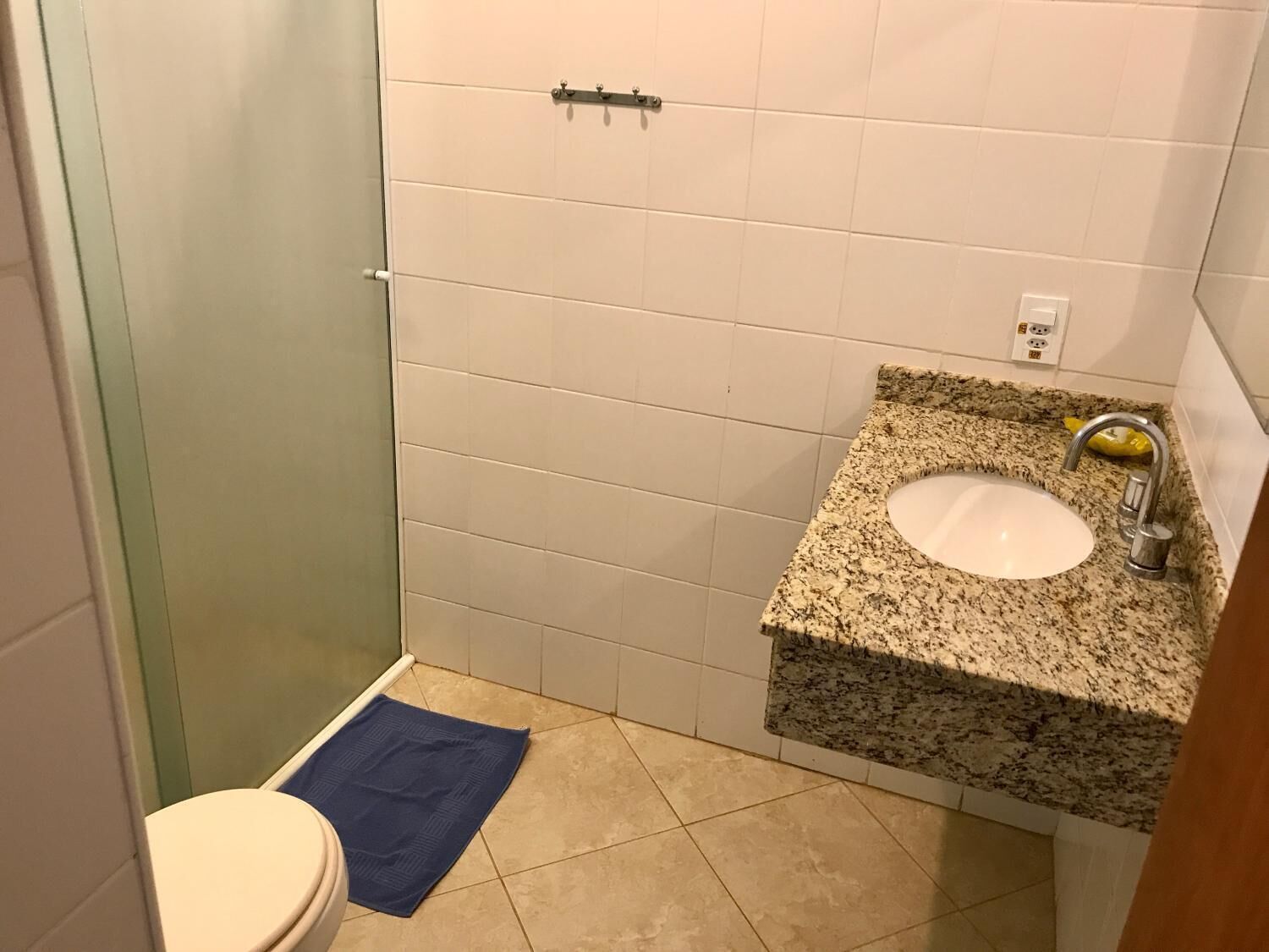 A bathroom with a white toilet, a blue bath mat, a granite sink, and a shower area.