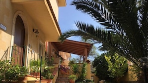 A courtyard with a paved walkway, potted plants, and a pergola. - Villa Rahal (Racalmuto)