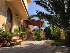 Un patio con sendero adoquinado, plantas en macetas y una pérgola.
