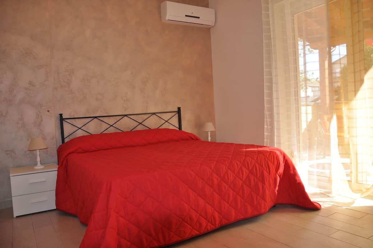 A bedroom with a bed, a nightstand, a lamp, and a window with curtains.