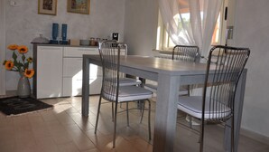 A dining area with a table and chairs, a vase with sunflowers, and a window with sheer curtains. - Villa Rahal (Racalmuto)