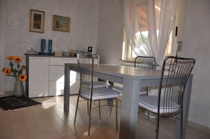 Un comedor con una mesa y sillas, un florero con girasoles, y una ventana con cortinas translúcidas.
