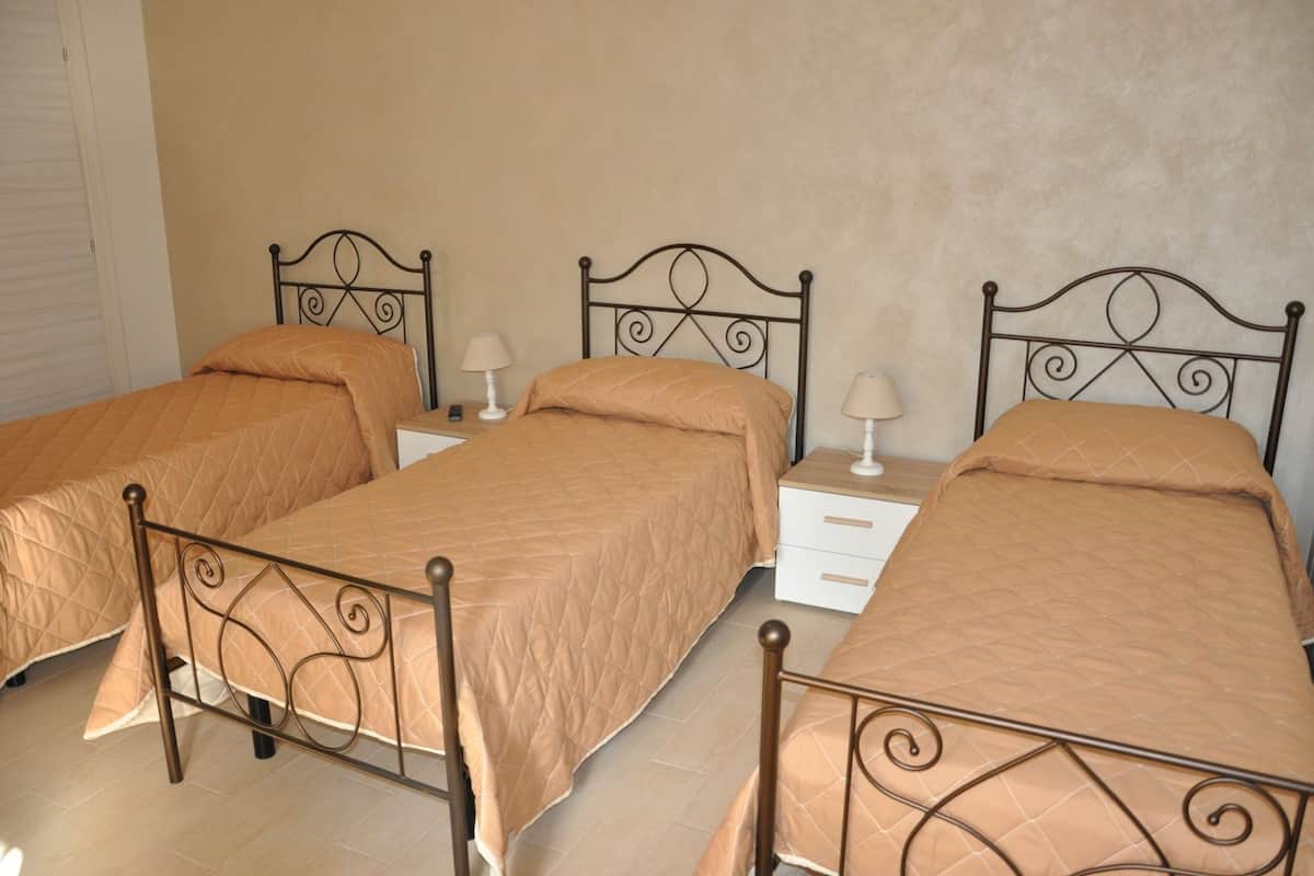 A room with three single beds, each with a matching headboard and footboard, and a bedside table with a lamp.