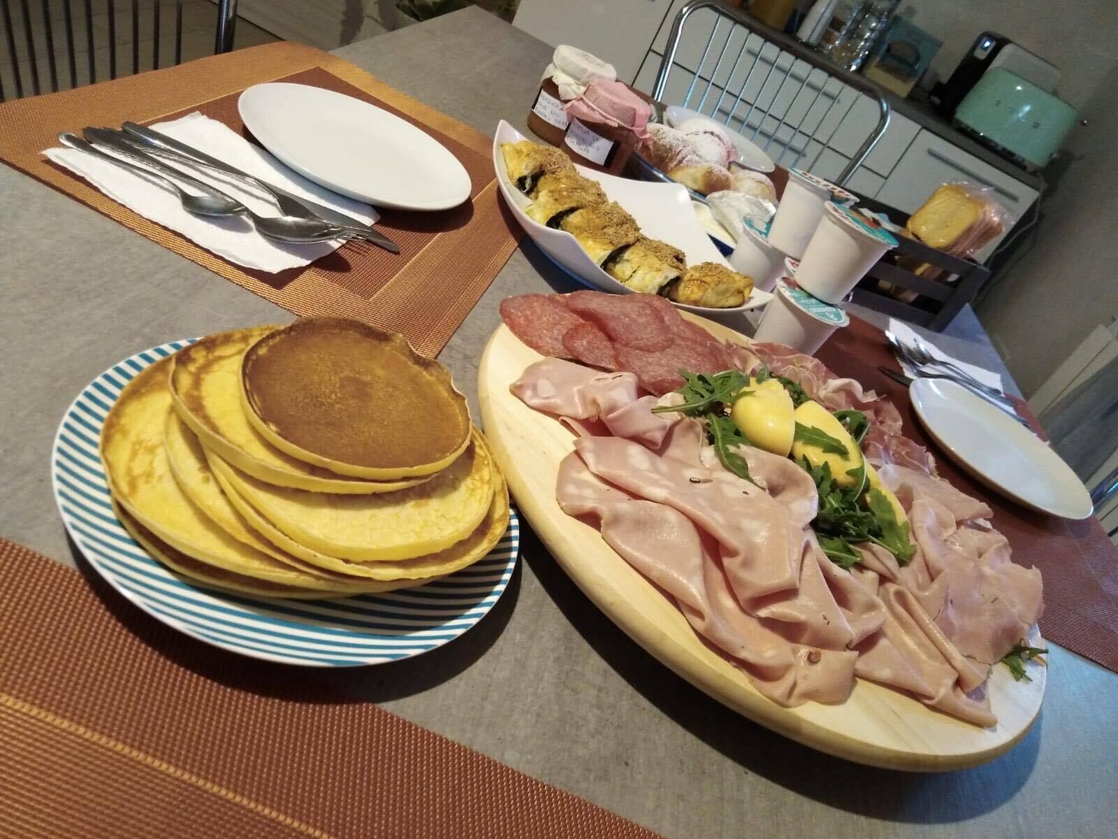 A breakfast setting with pancakes, ham, and pastries on a table.