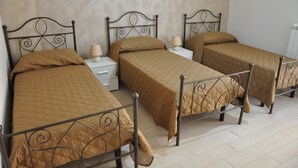 A room with three single beds, each with a metal frame and a brown quilted bedspread. There are bedside tables with lamps and a white wall in the background. - Villa Rahal (Racalmuto)