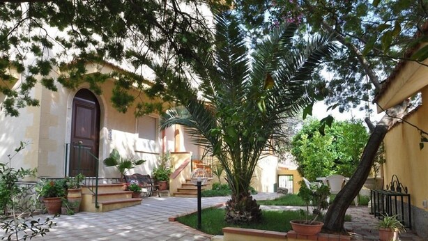 A courtyard with a tiled floor, a palm tree, potted plants, and a staircase leading to an upper level. - Villa Rahal (Racalmuto)