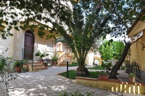 A courtyard with a tiled floor, a palm tree, potted plants, and a staircase leading to an upper level. - Villa Rahal (Racalmuto)